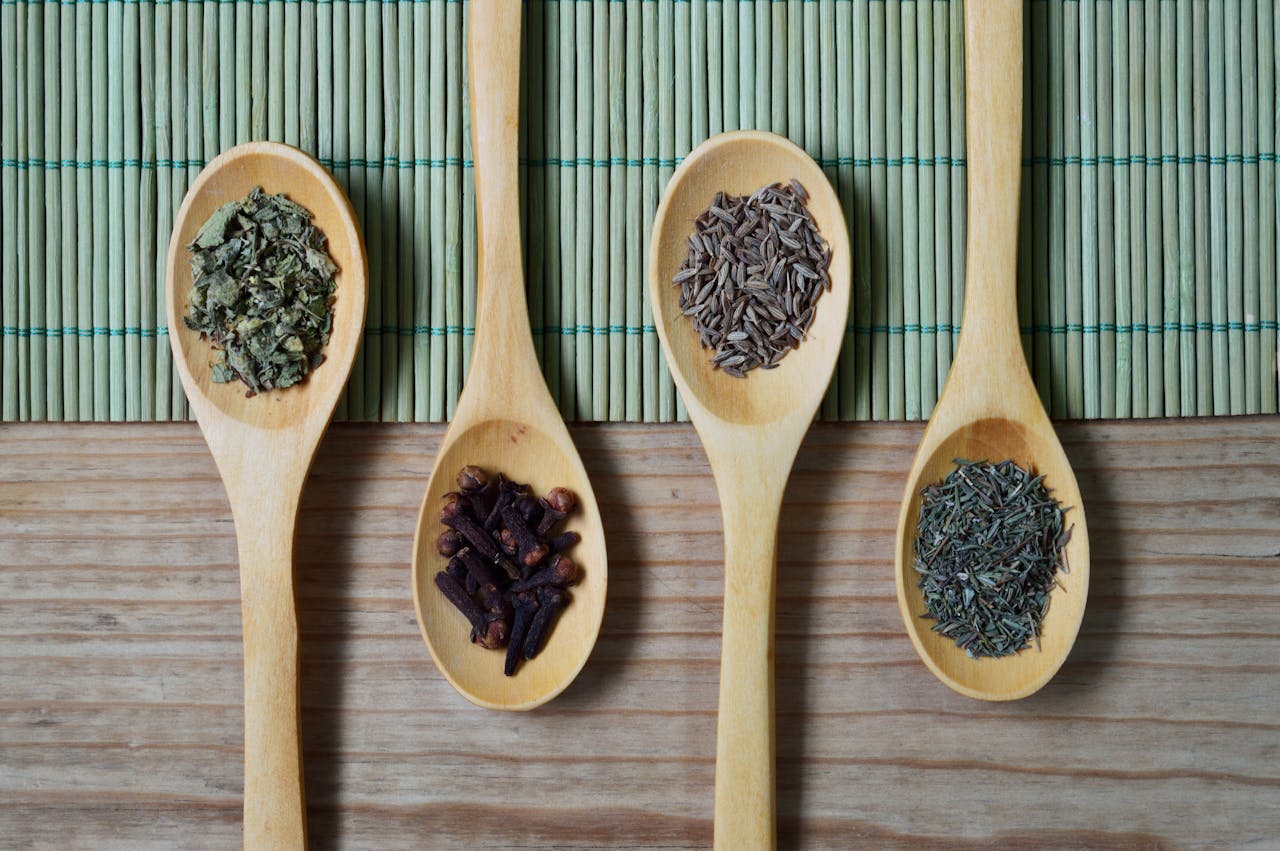 about-01 Overhead view of wooden spoons filled with spices and herbs on a bamboo mat, ideal for culinary themes.