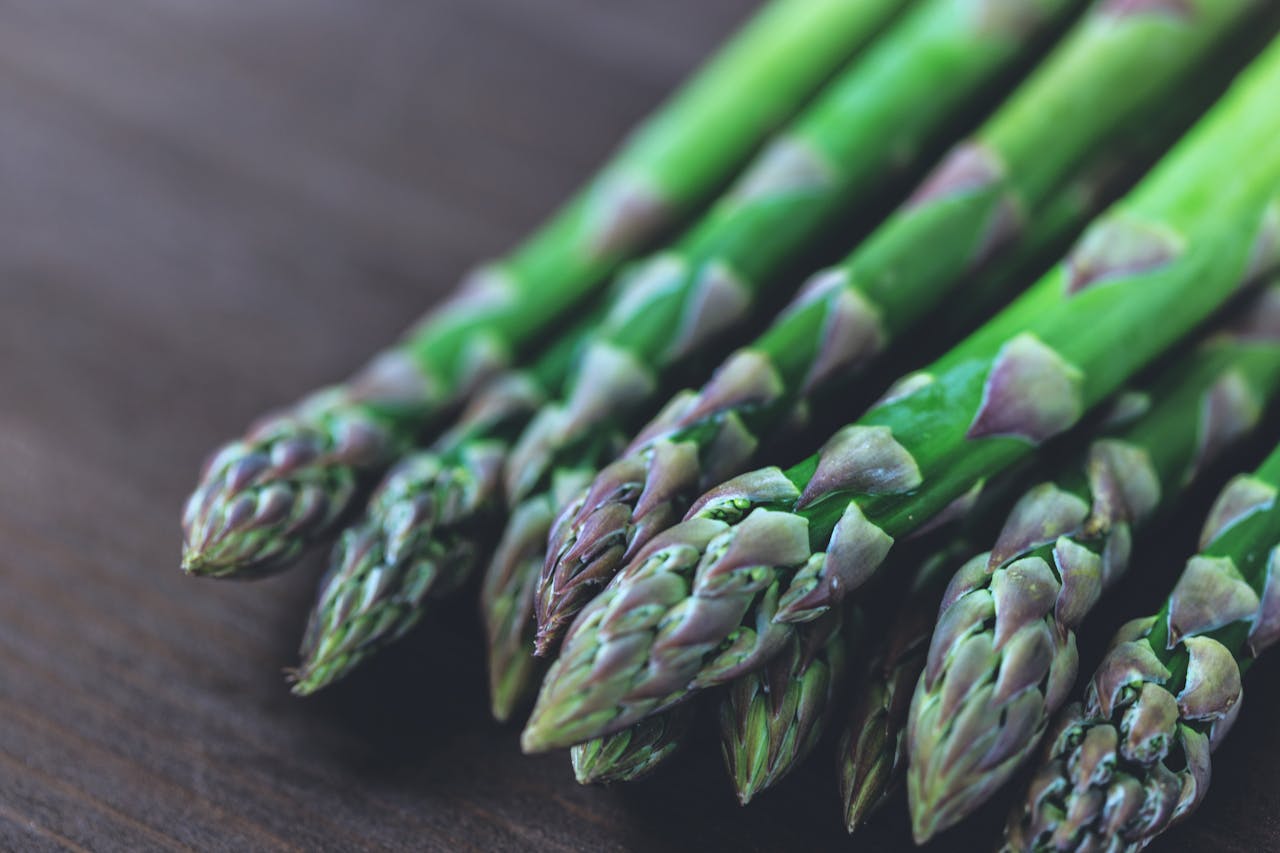 gallery-3 Close-up of fresh green asparagus spears displayed on a rustic wooden table.